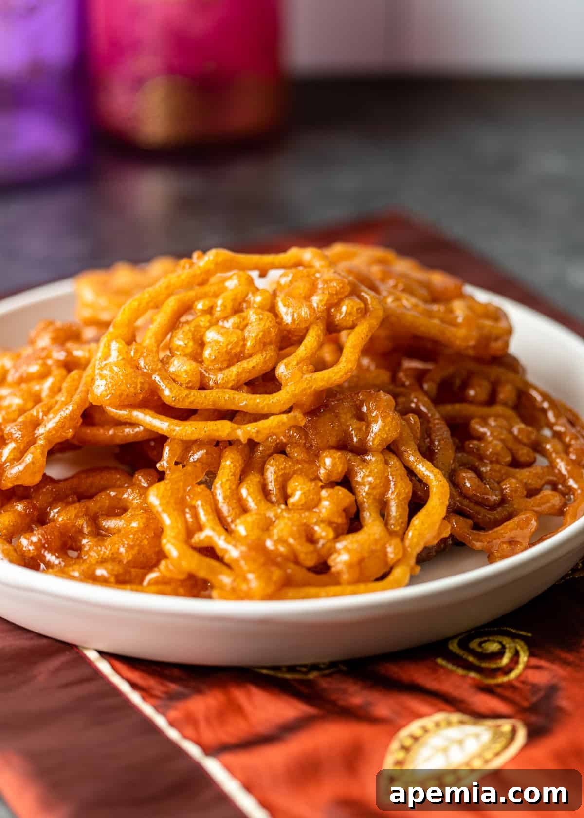 side view of a plate filled with a mound of crispy, syrupy jalebi, showcasing its texture