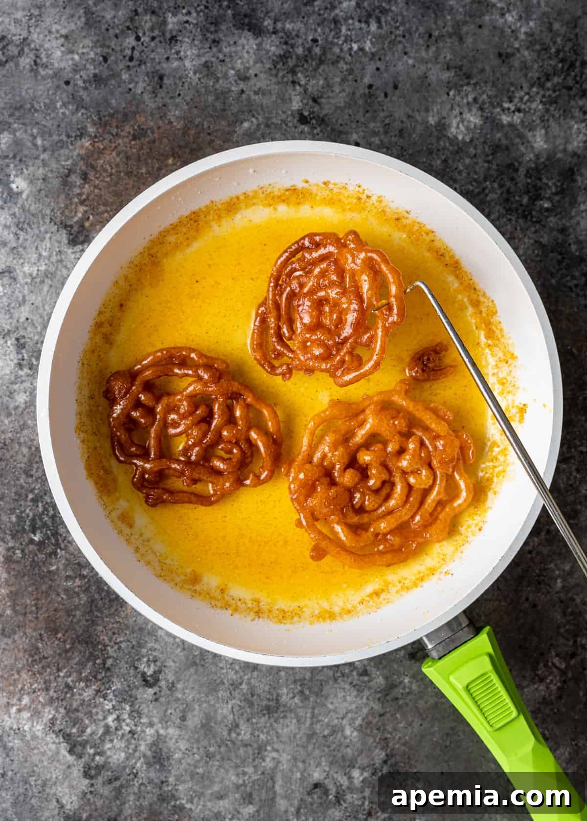 overhead shot of soaking hot jalebi in warm sugar syrup in a skillet, turning to coat