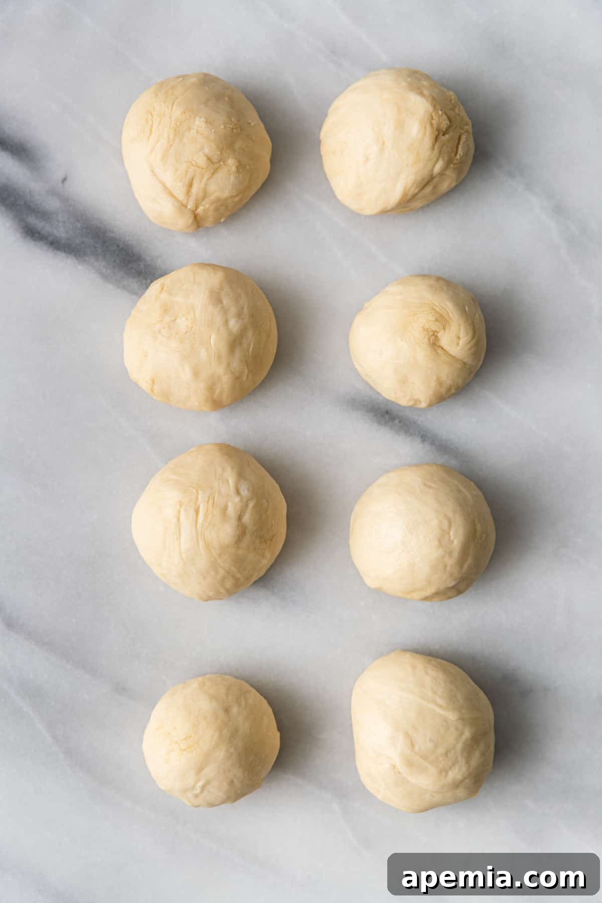 Overhead shot of 8 neatly rolled naan dough balls arranged on a baking sheet, ready for their final short rise.