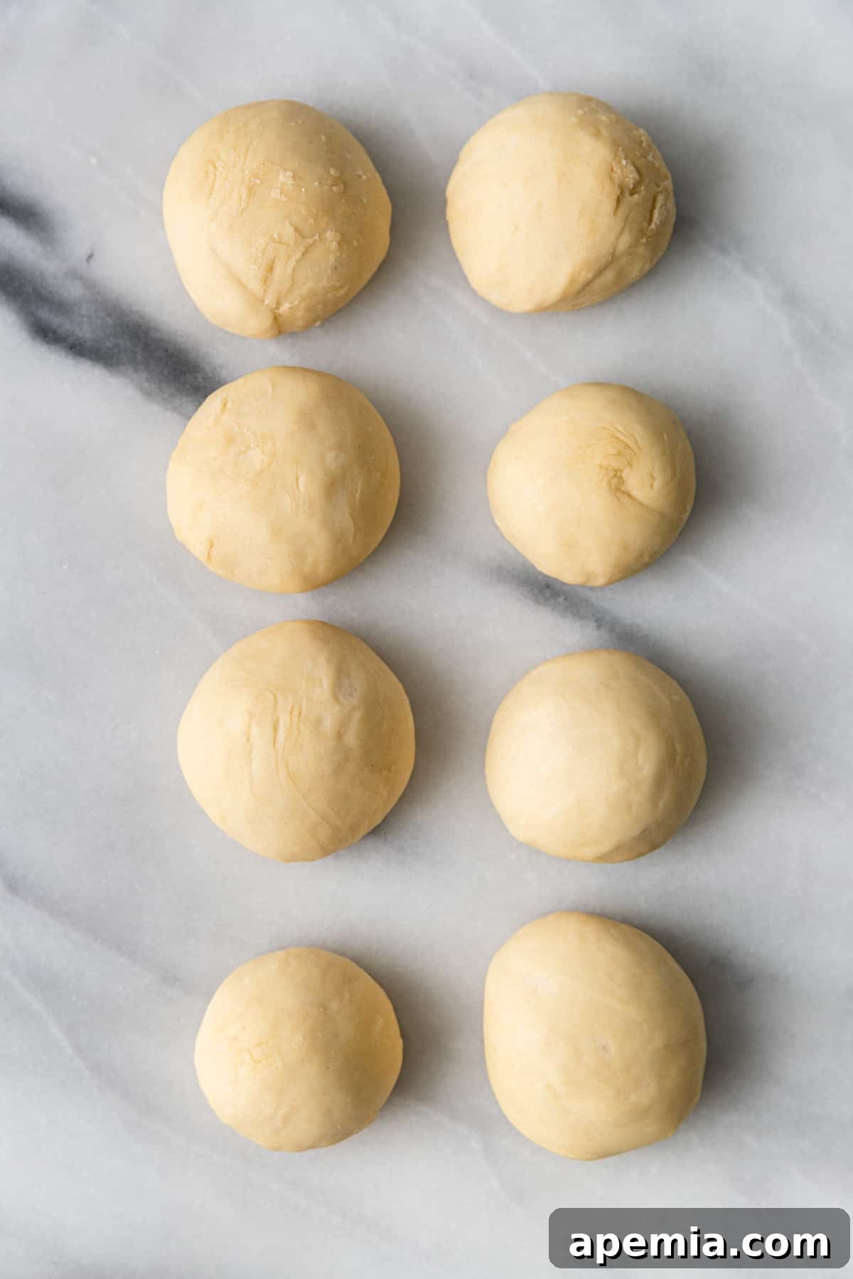 Overhead shot of 8 risen and plump naan dough balls on a tray, showing the results of the second proofing.