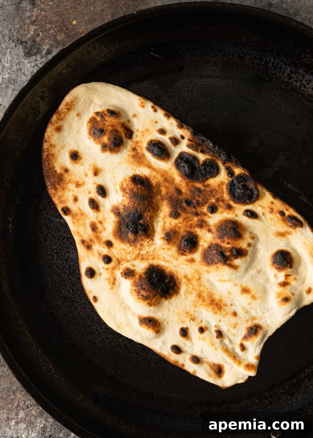 A piece of Indian flatbread with beautiful char marks and blisters in a skillet, having just been cooked over an open flame or broiler.