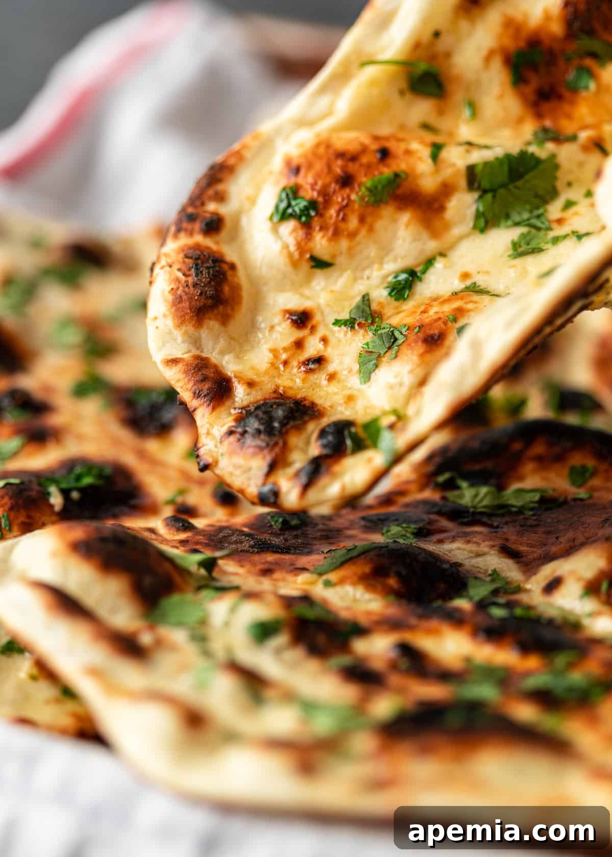 A hand reaching to pick up a piece of warm garlic naan adorned with fresh cilantro from a tray.