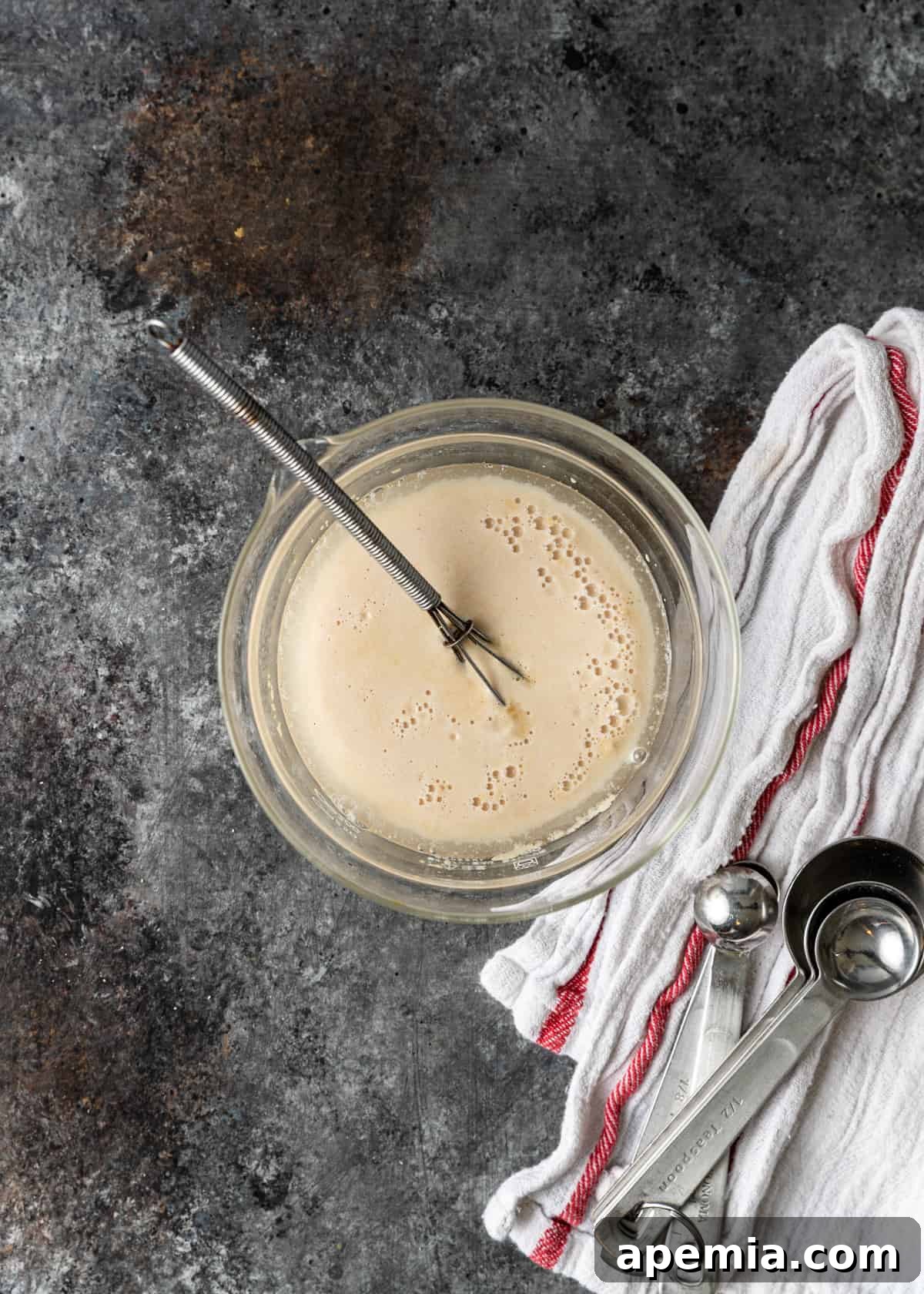 Overhead shot showing the yeast mixture gently activating in a bowl, beginning to show small bubbles.