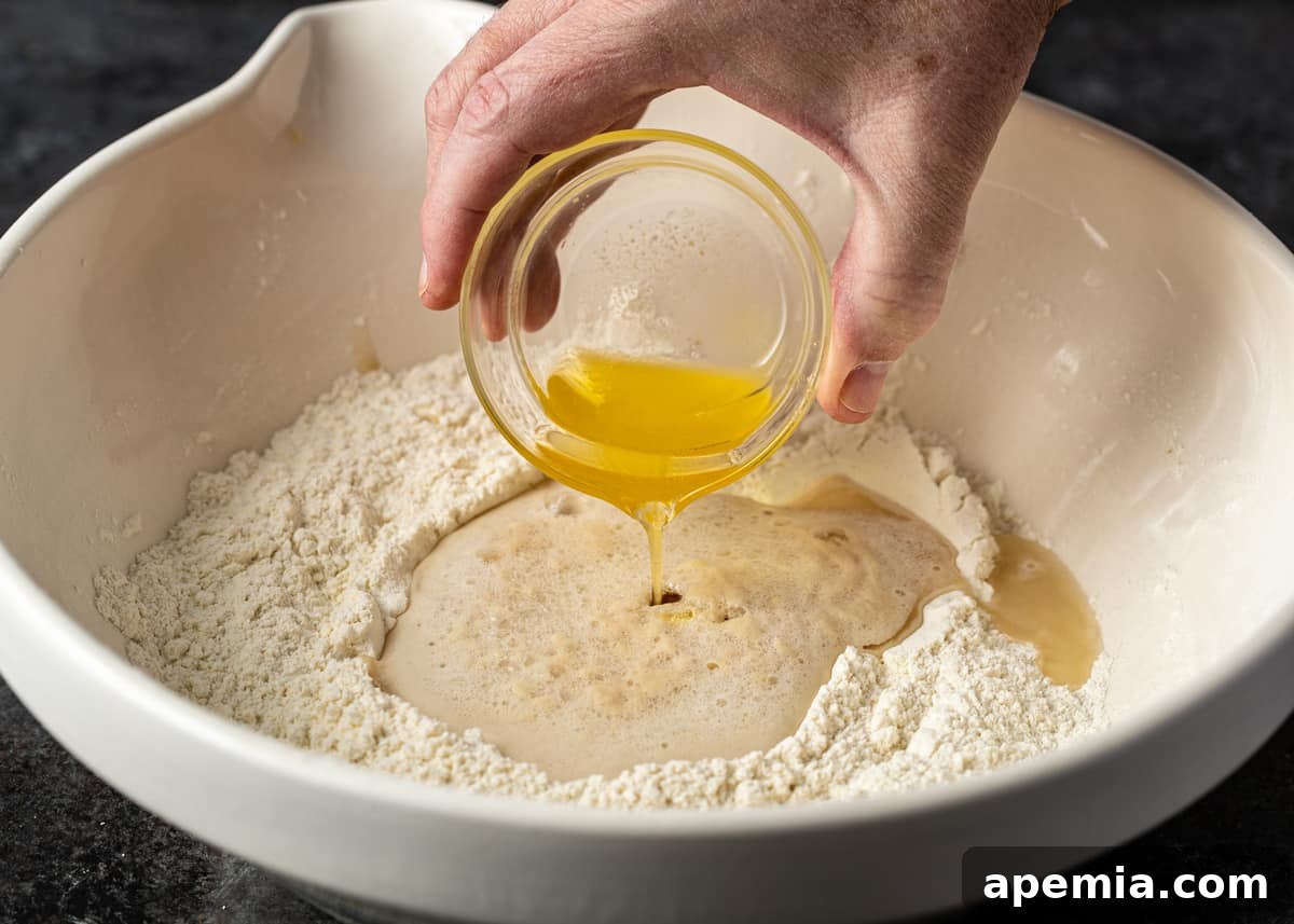 Overhead shot of melted ghee being poured into the naan dough mixture in a large mixing bowl.