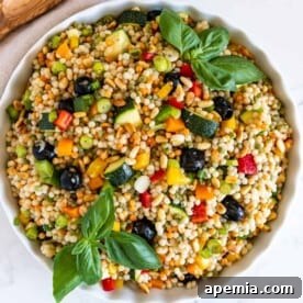 Overhead image of a bowl of Ptitim (Israeli couscous salad) with fresh ingredients.