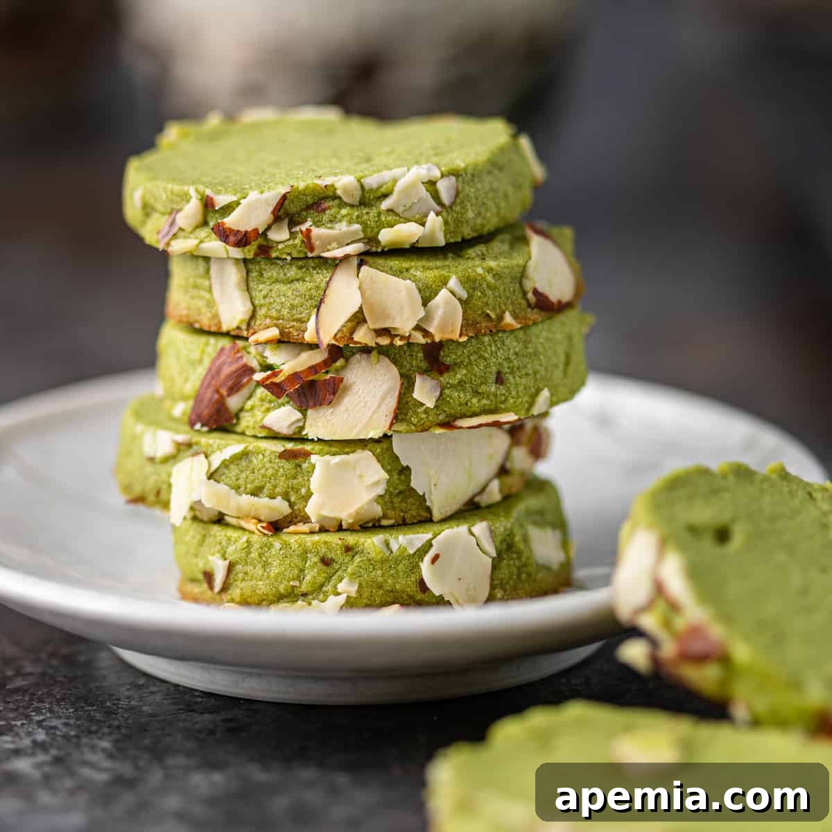 Closeup side view of a stack of vibrant green matcha cookies on a white plate, with a few cookies artfully placed to the side.
