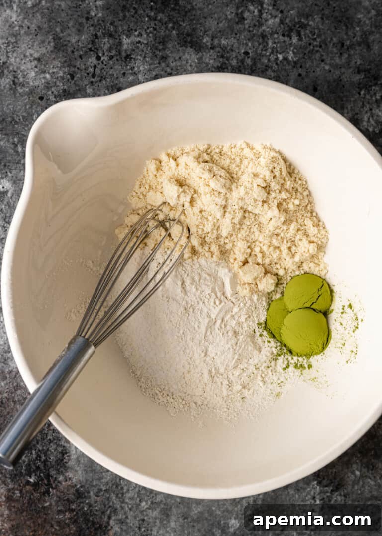 Overhead process shot: mixing together dry ingredients, including all-purpose flour, almond flour, matcha powder, and salt, in a separate bowl.