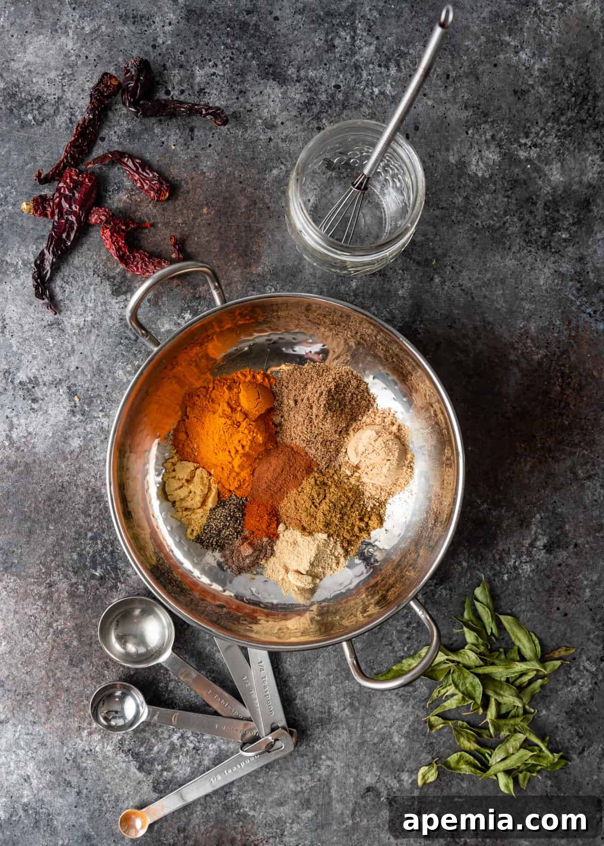 A collection of whole spices, including dried Kashmiri chiles, cardamom pods, and cumin seeds, laid out for making Madras Curry Powder.