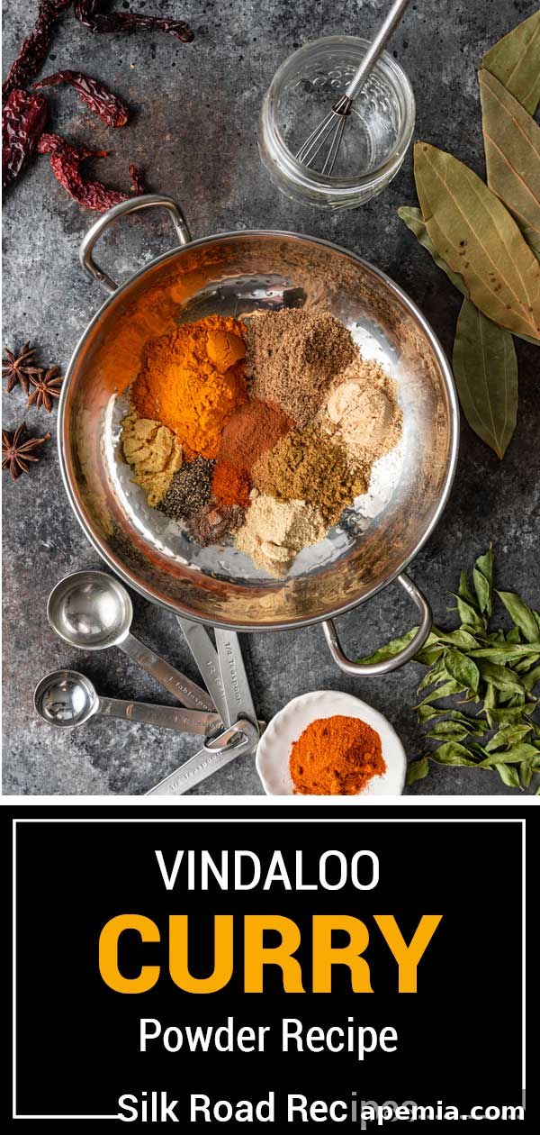 Overhead shot of vibrant red Vindaloo Curry Powder in a small white bowl with a wooden spoon