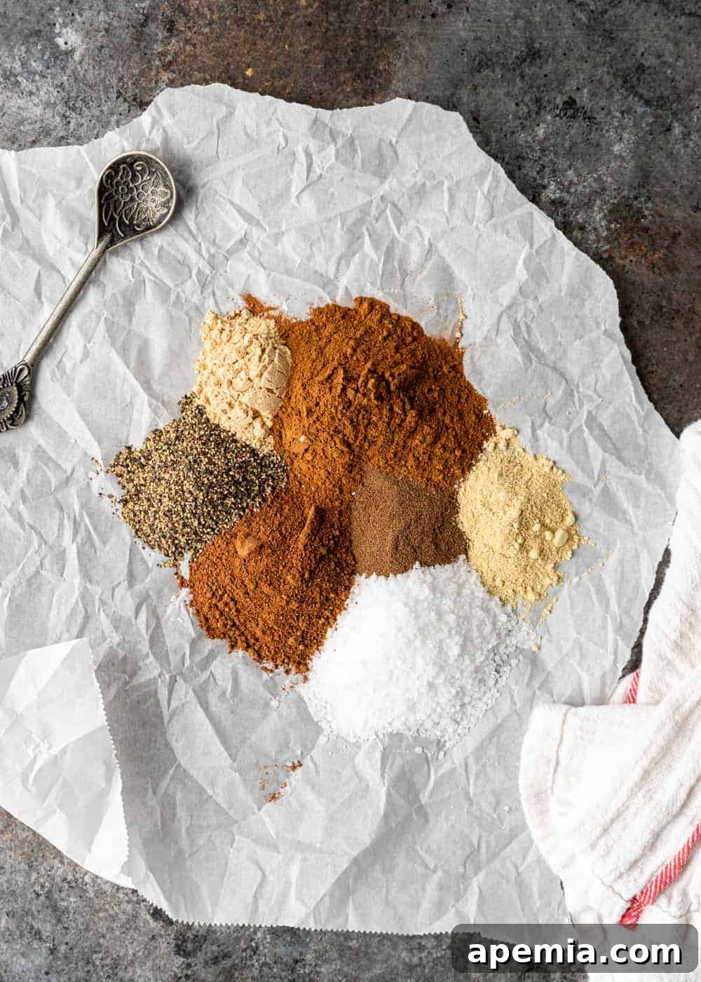 Overhead shot of individual spices for Lebanese seven spice blend arranged on a piece of parchment paper, including cinnamon, nutmeg, fenugreek, and black peppercorns.
