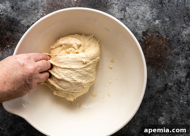 Beloved Turkish Ramadan Pide 13 A hand gently pressing down on the dough in the bowl, completing a fold.
