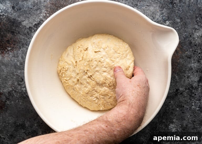 Beloved Turkish Ramadan Pide 9 A hand with wet fingers gently picking up a portion of the risen dough, preparing for folding.