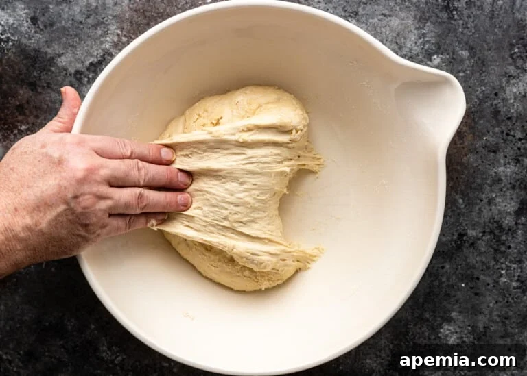 Beloved Turkish Ramadan Pide 10 A hand gently pulling a section of the dough upwards and towards the baker, demonstrating the stretch and fold technique.