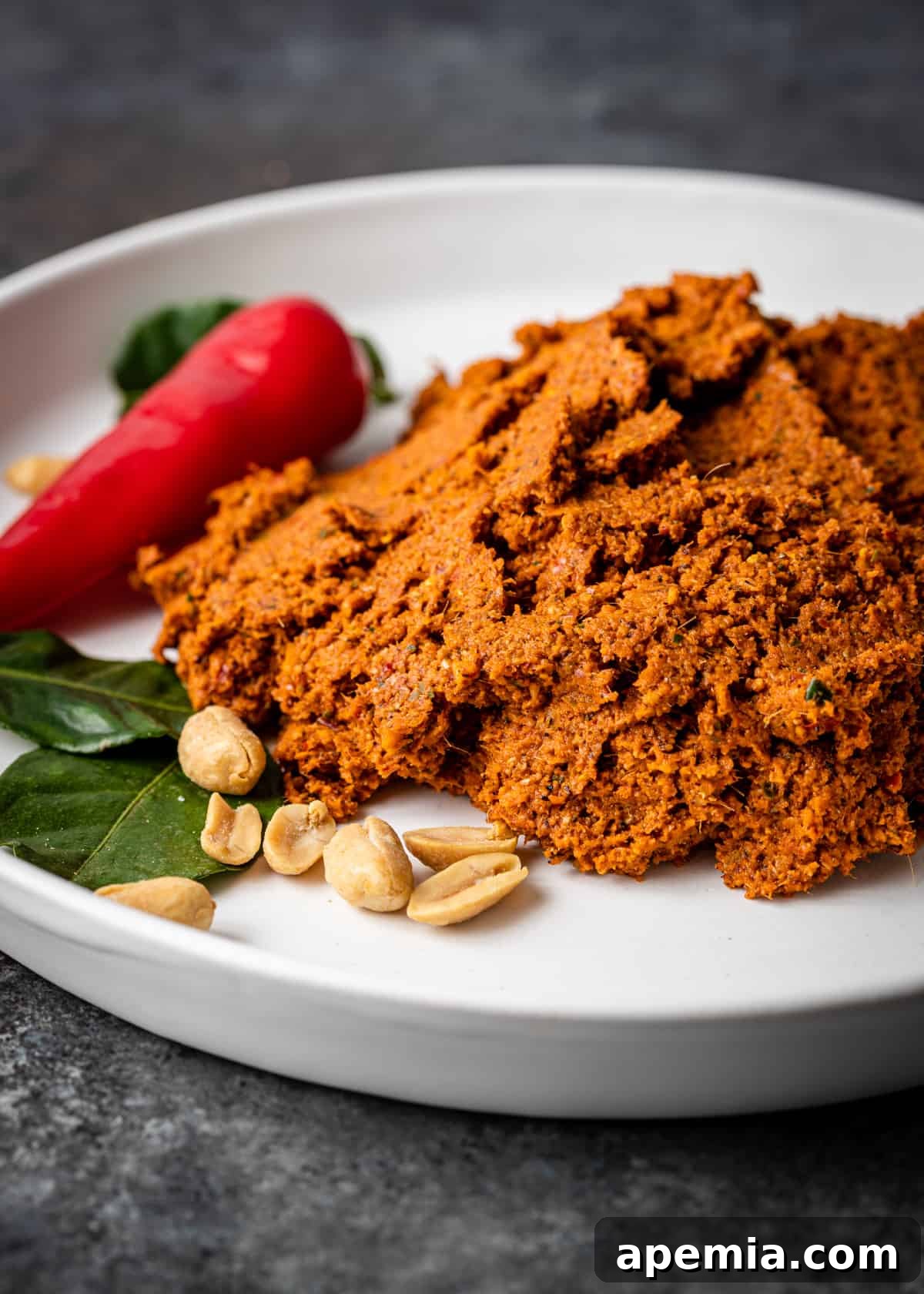 closeup side view: red chili and peanuts on a white plate with a dollop of panang curry paste