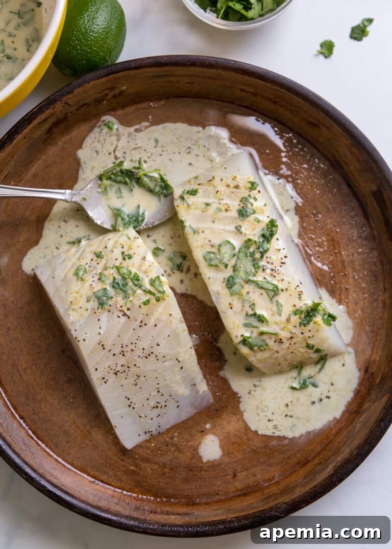 Overhead view of two raw halibut pieces coated in green curry sauce in a baking dish, before baking.