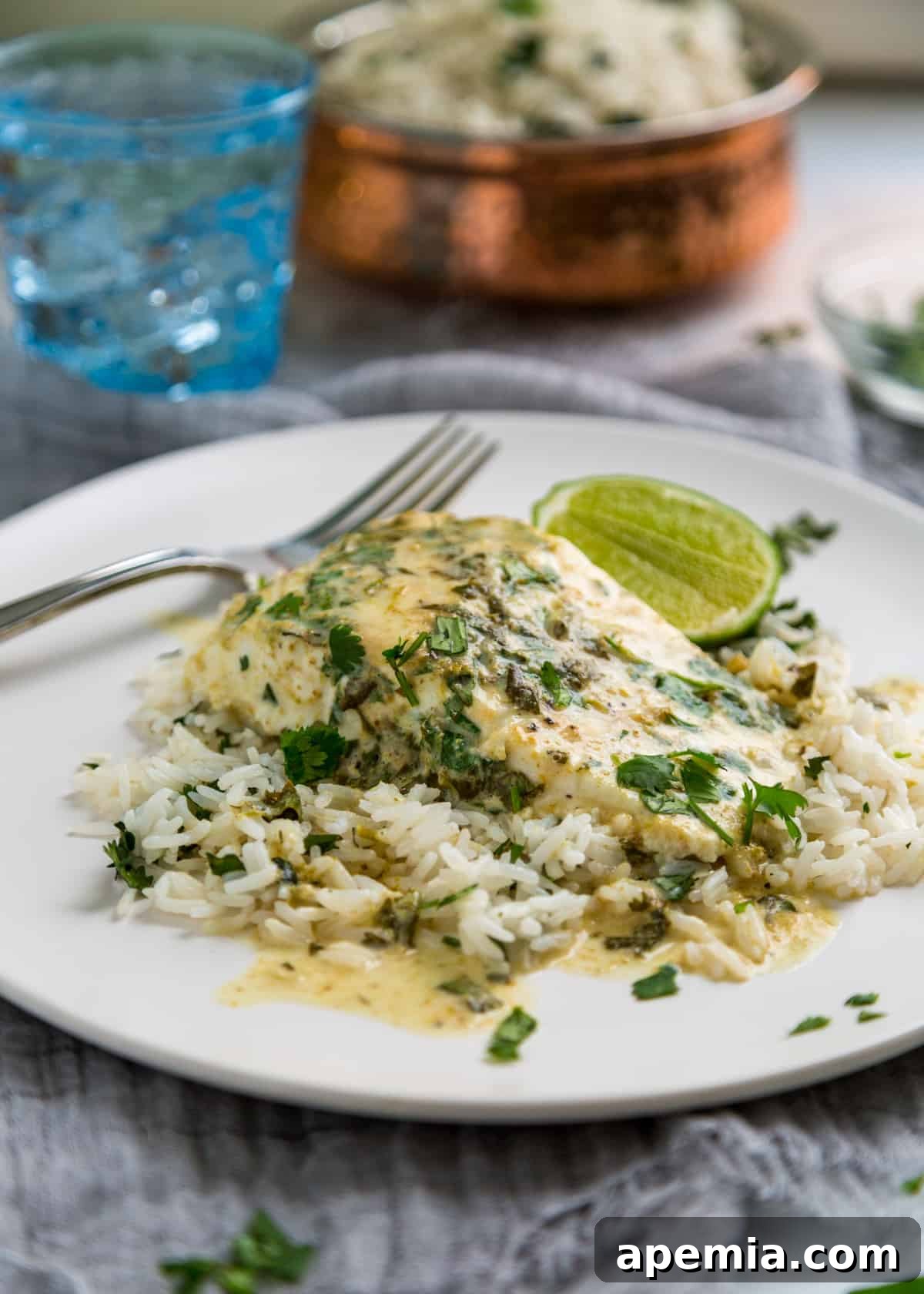 Side view closeup of a baked halibut fillet covered in vibrant green curry sauce, served over coconut rice with a fresh lime wedge on the side.
