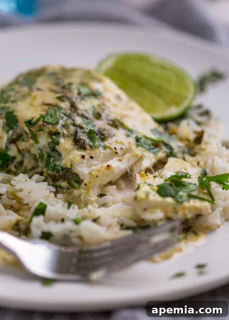 Extreme closeup of a perfectly cooked piece of green curry fish on a white plate, showcasing its flaky texture, with a fork and a lime wedge ready for enjoyment.