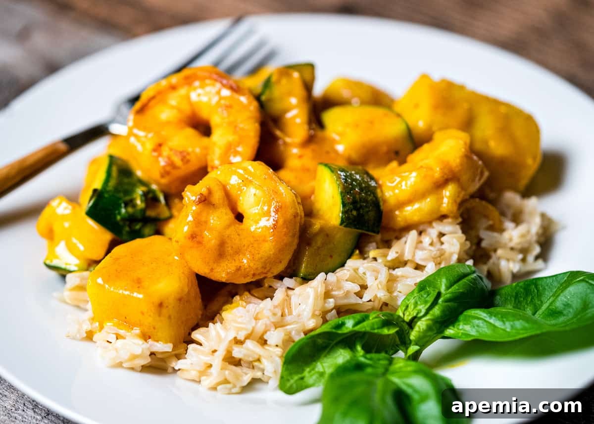 Side view of a plate with Thai yellow shrimp curry, steamed rice, and fresh Thai basil leaves for garnish.