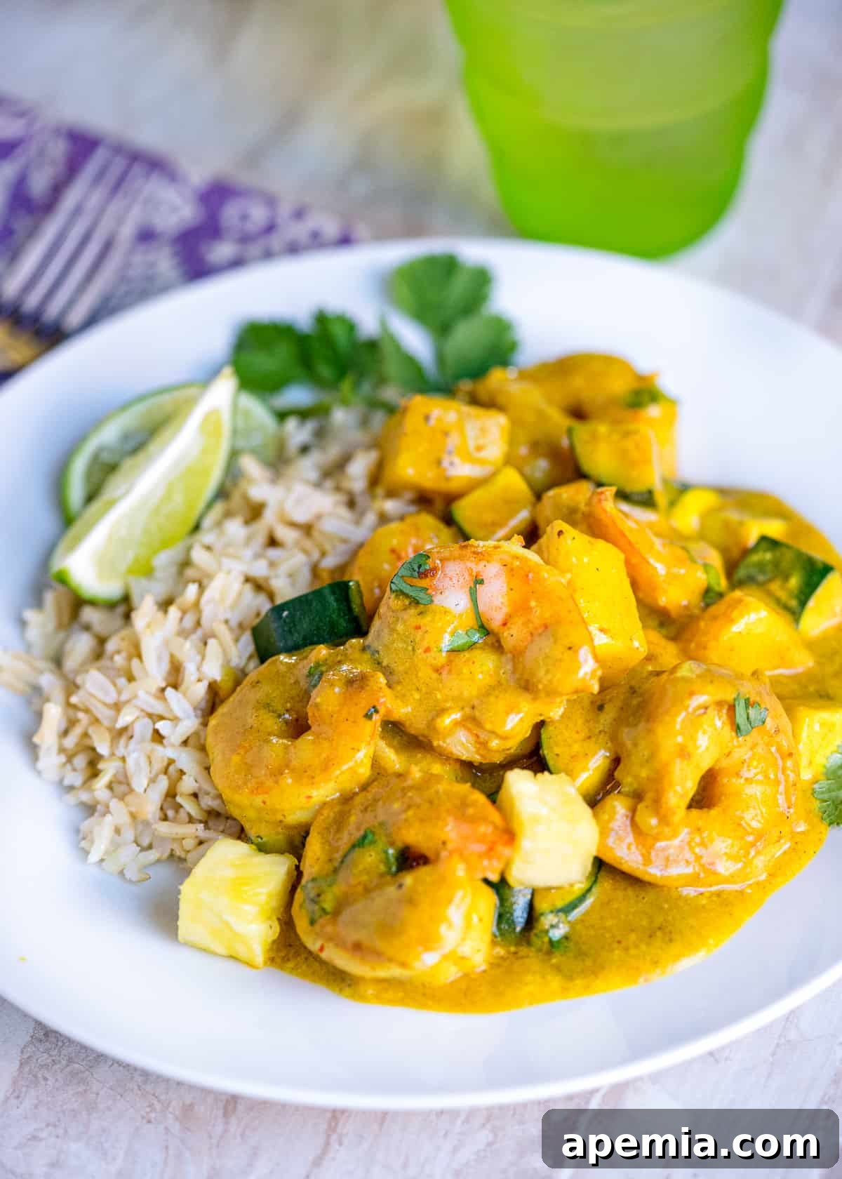 Closeup of a generous serving of Thai coconut shrimp curry with rice and lime wedges, beautifully plated.