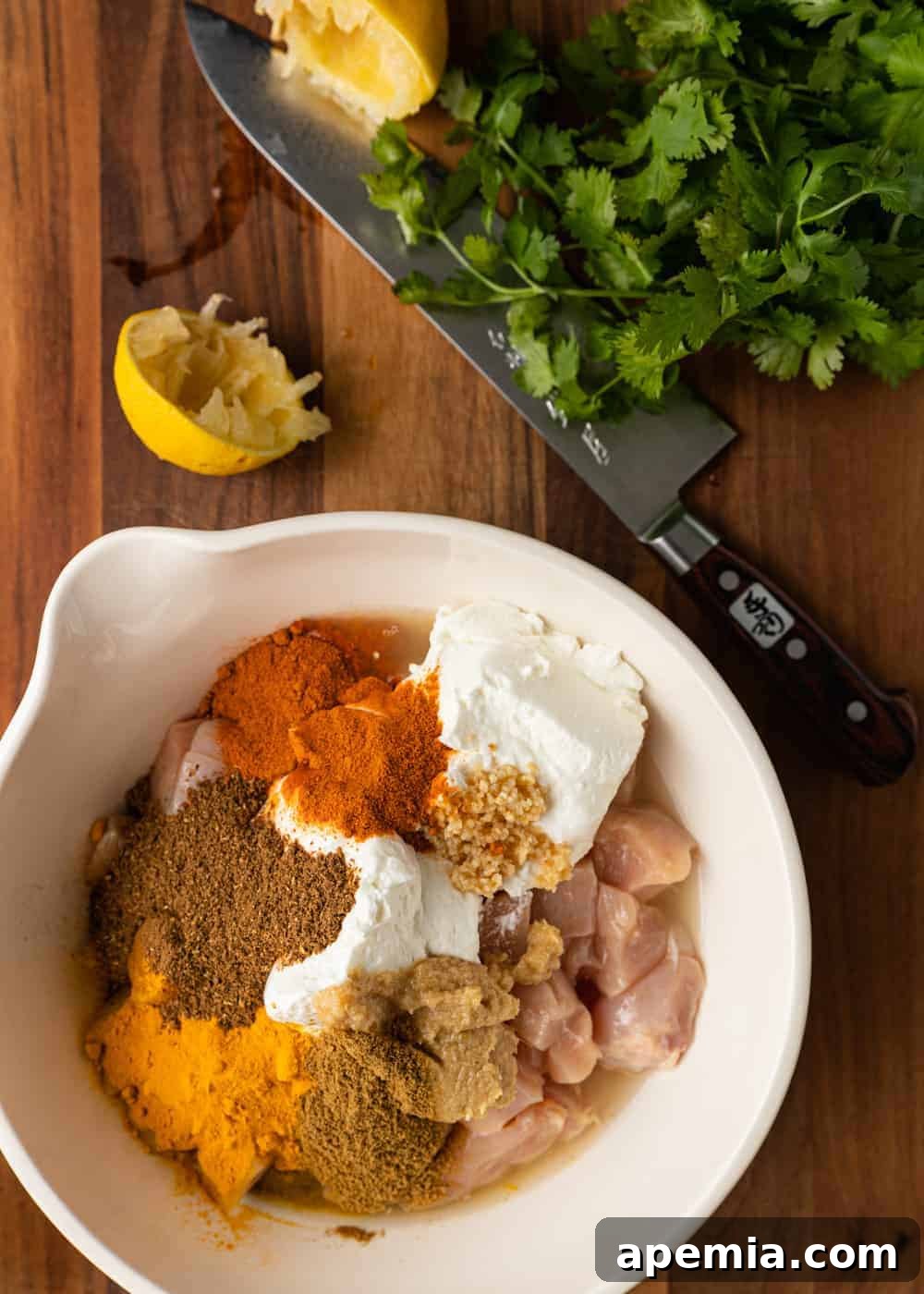 overhead photo: spices and raw chicken breast pieces in large white bowl for butter chicken recipe