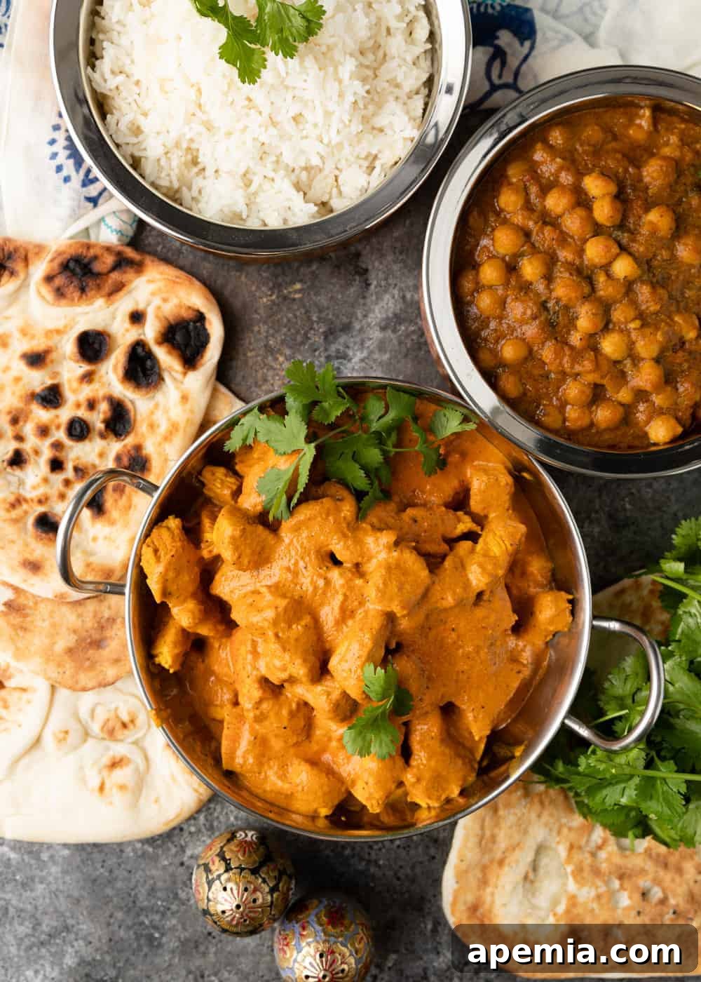 overhead of butter chicken, naan, rice and chickpea curry in copper bowls