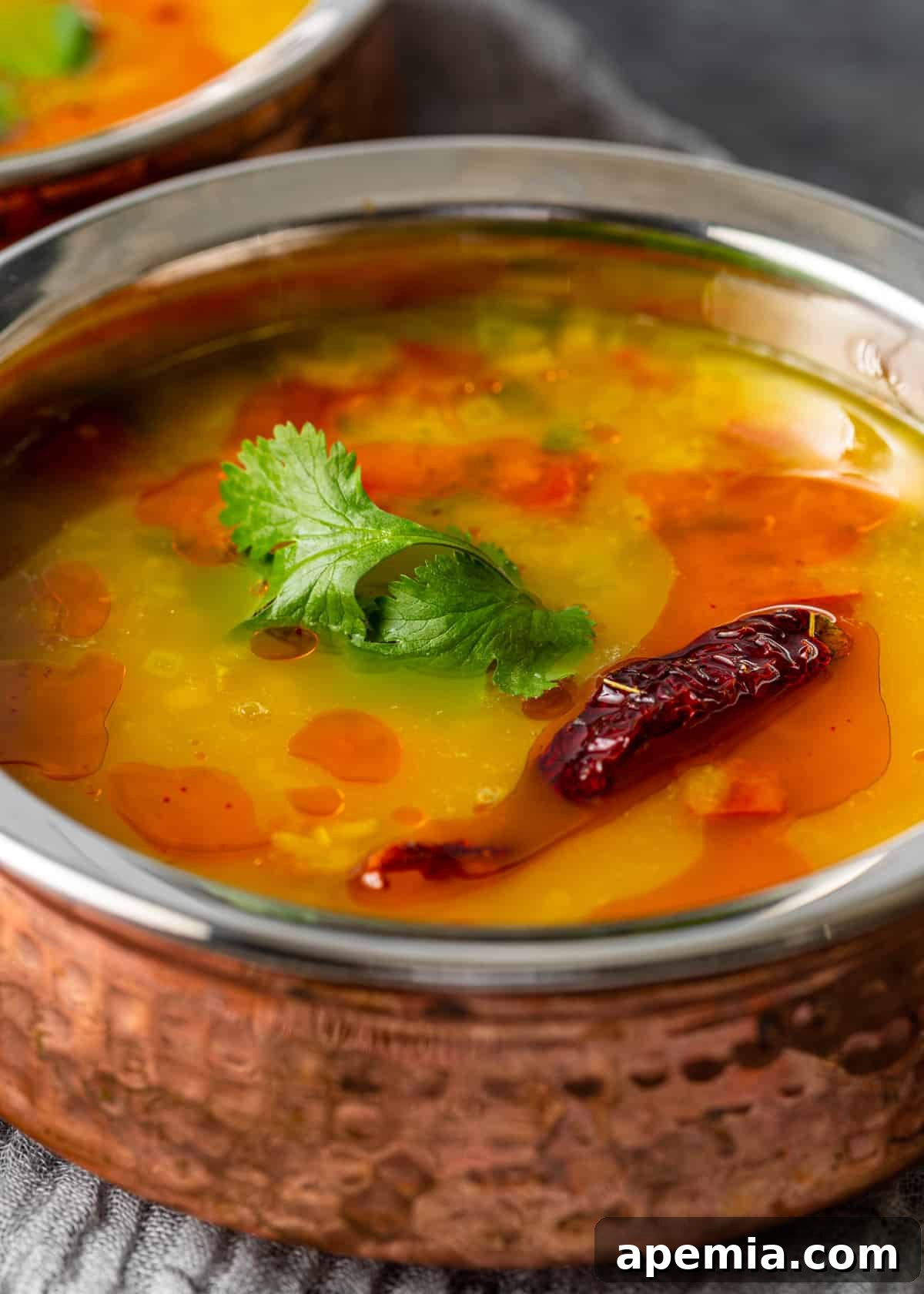 A close-up side view showcasing a single bowl of Dal Tadka, its creamy texture visible, with a hint of the flavorful tadka on top. It sits on a hand towel, highlighting its inviting appearance and readiness to be savored.