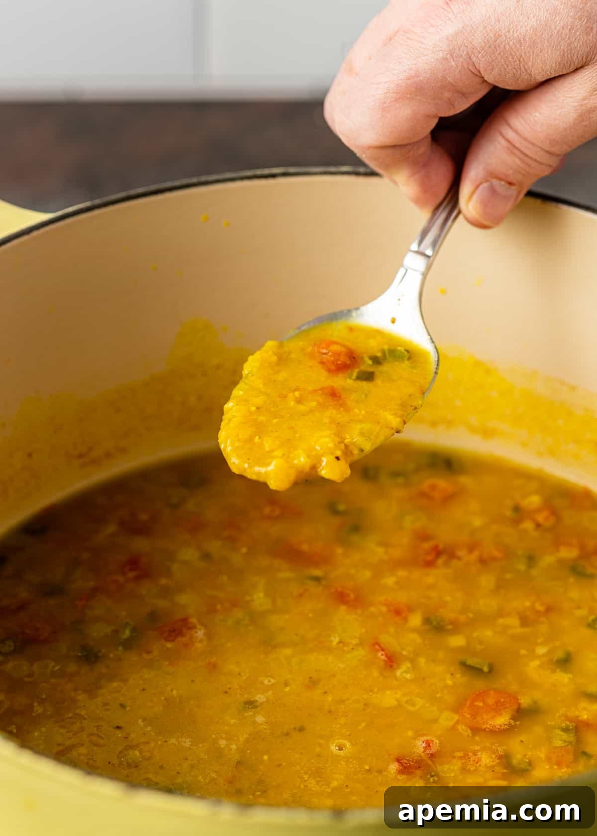 A hand gently scooping a spoonful of creamy, golden Dal Tadka from a rustic bowl, showcasing the inviting texture and steaming warmth. A subtle sprinkle of fresh herbs adds a touch of color.