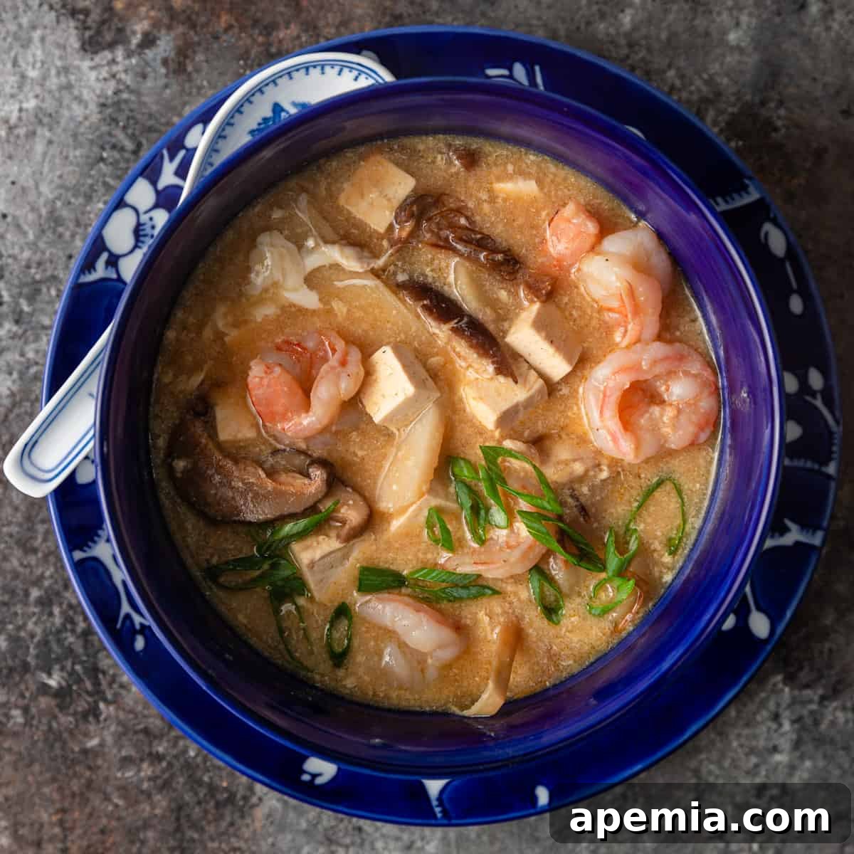 An overhead shot of a vibrant blue bowl filled with homemade hot and sour soup, garnished with green onions.