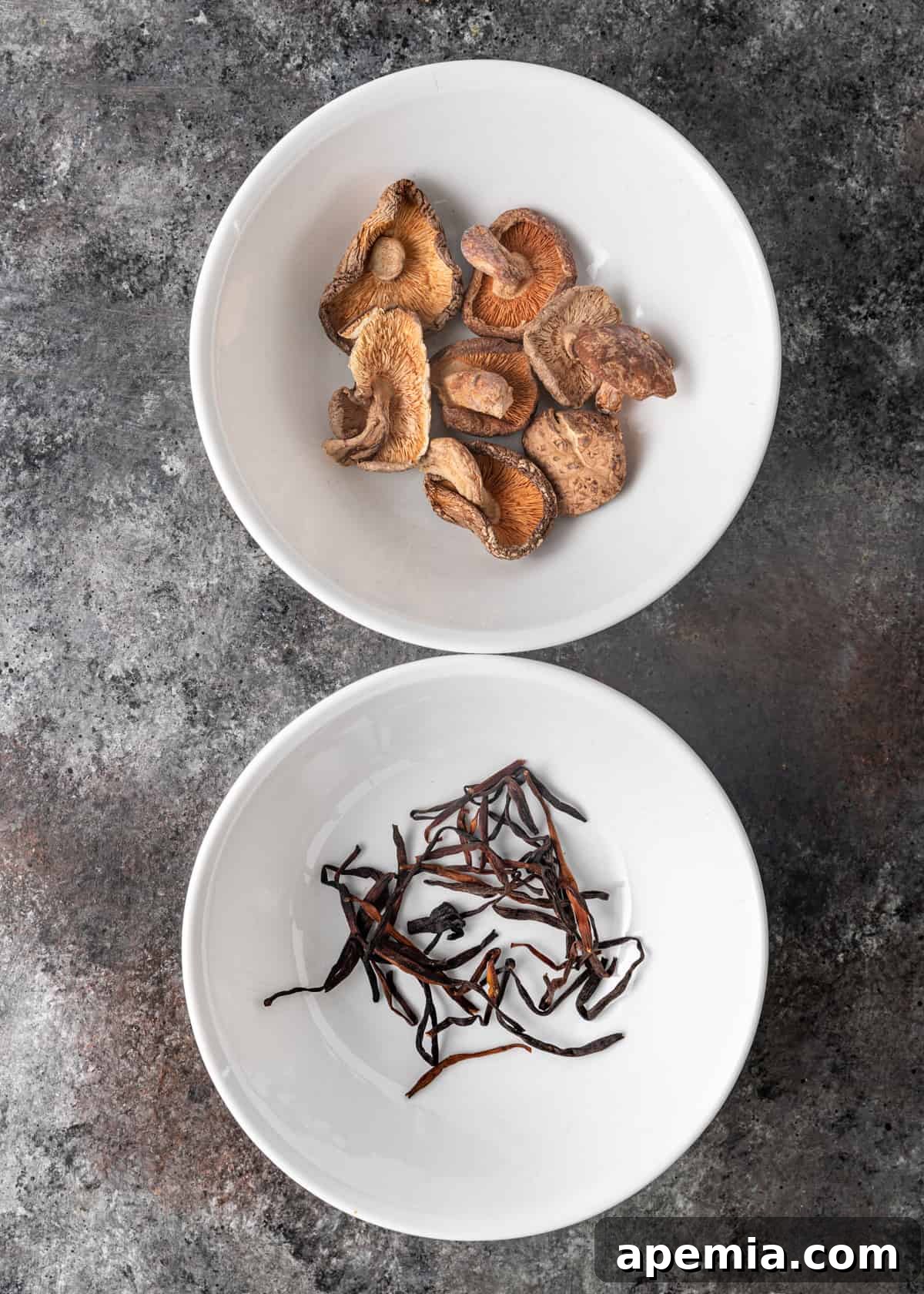 Overhead view of dried shiitake mushrooms and dried lily flowers in white ceramic bowls, essential ingredients for hot and sour soup.