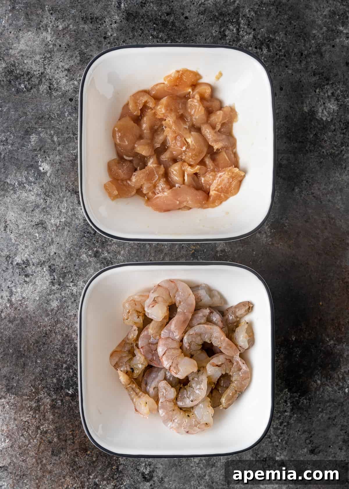 Overhead view of marinated chicken and shrimp, prepared in separate bowls, ready to be added to the hot and sour soup.