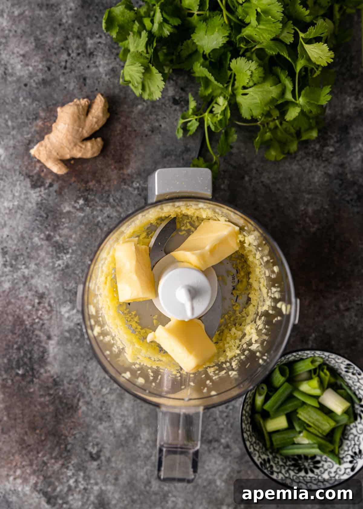Scallion, ginger, and softened butter being combined in a food processor to create the aromatic butter