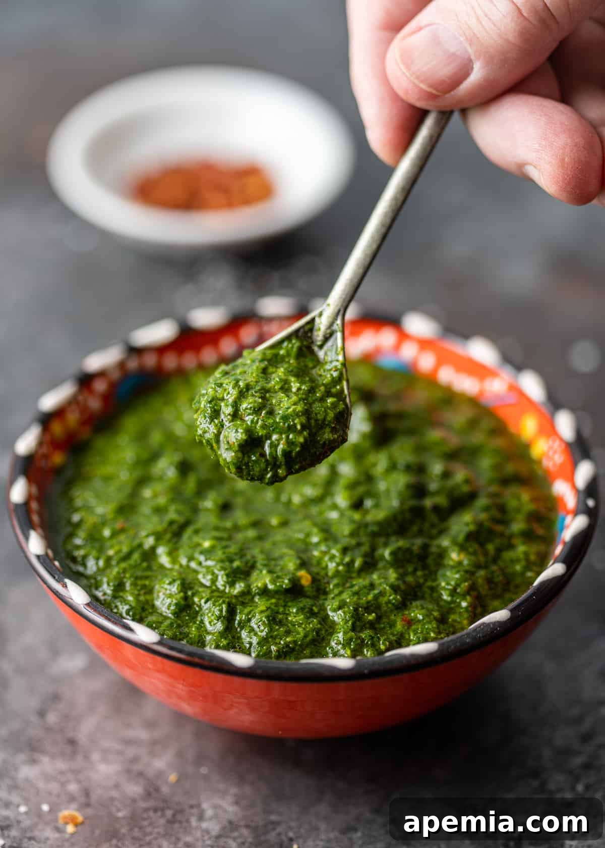 Close-up: a hand lifting a spoonful of vibrant green chermoula, highlighting its smooth texture and fresh color.