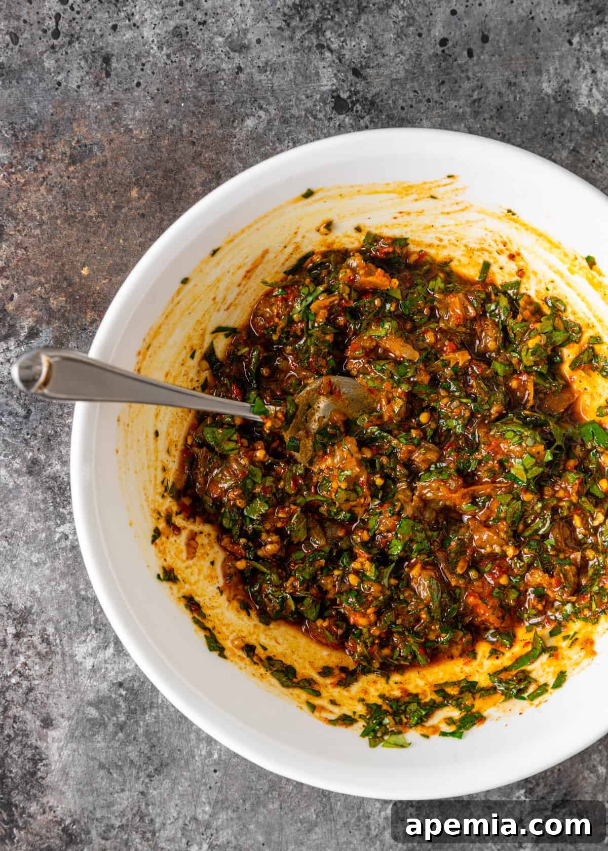 Overhead view: all the stirred ingredients for red chermoula combined in a bowl, showing a rich, chunky texture.