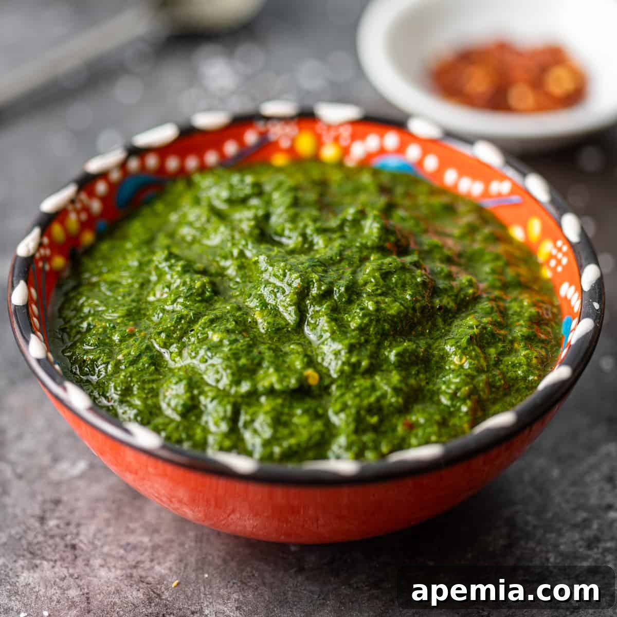 Close-up: a small, colorful ceramic bowl filled with vibrant green chermoula, highlighting its fresh, herbaceous quality.