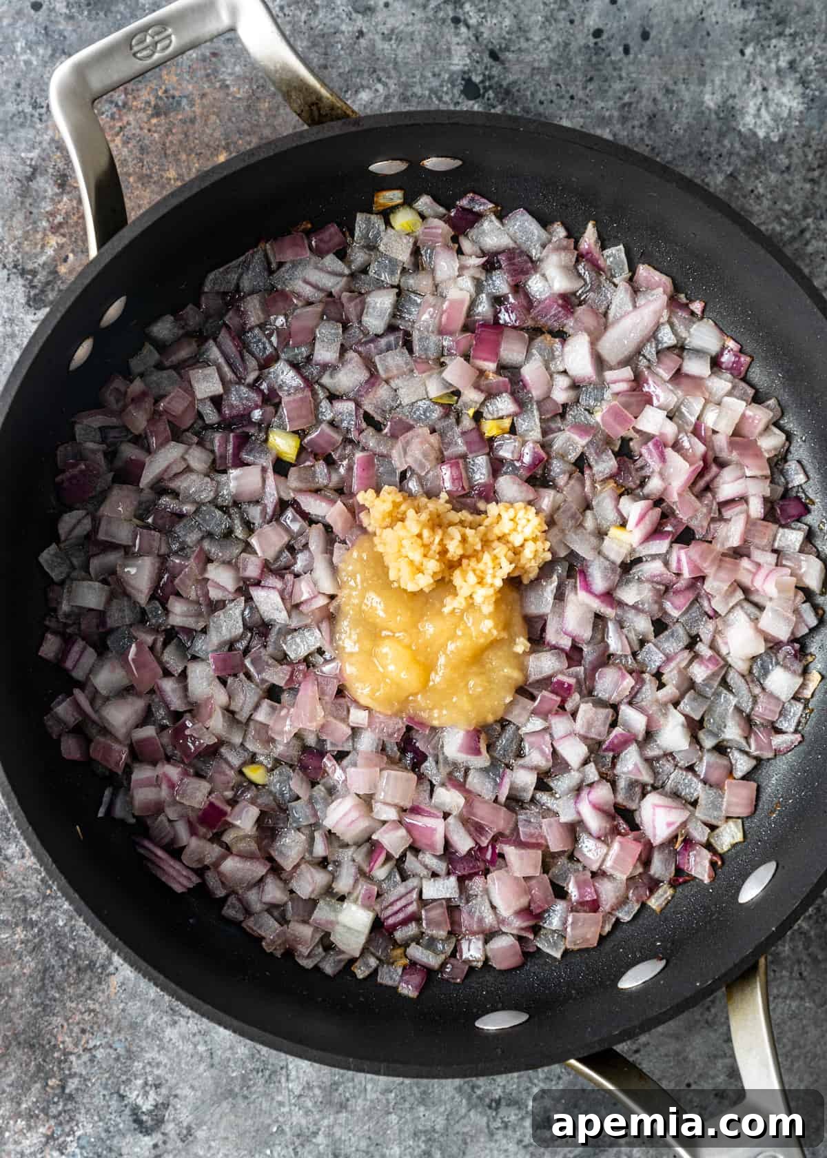 Overhead process shot: Sautéing finely chopped red onion, minced garlic, and ginger paste in a skillet until fragrant and translucent.