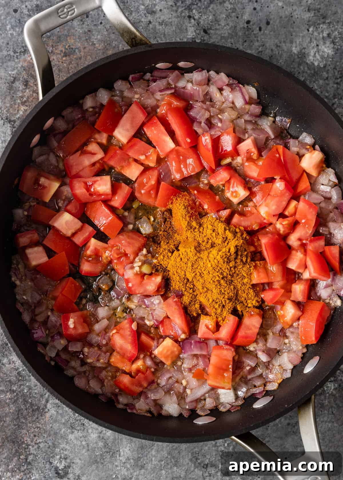 Overhead process shot: Adding chopped Roma tomatoes and fragrant curry powder to the skillet, stirring to combine for the flavor base.