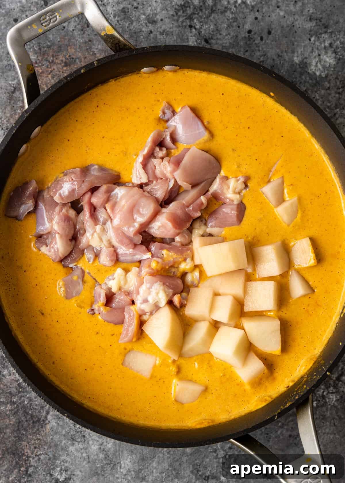 Overhead process shot: Adding tender chicken pieces and cubed white potatoes to the simmering curry sauce, ensuring they are well coated.