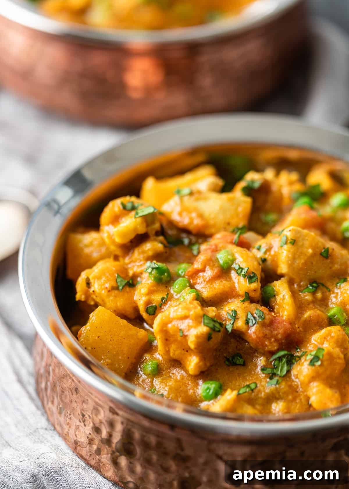 Closeup side view of creamy Indian chicken curry in a bowl, showcasing its vibrant spices and tender chicken chunks against the rich sauce.