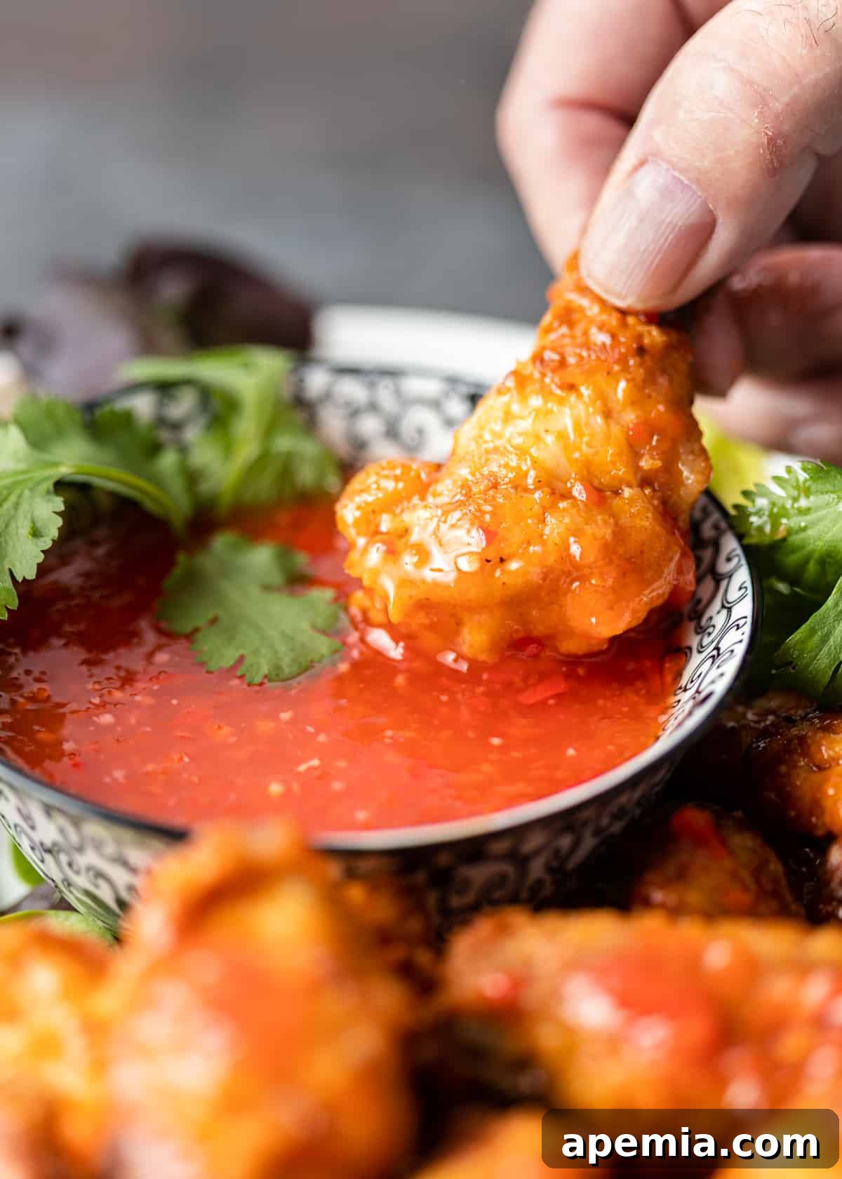 closeup: hand dipping chicken into chili sauce