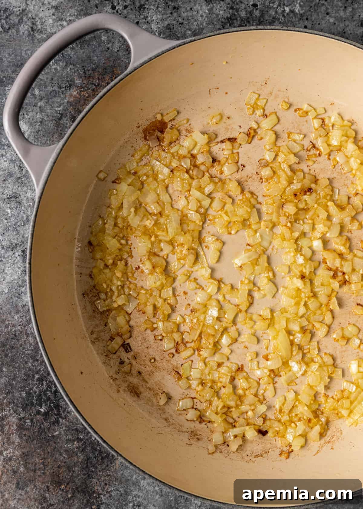 A close-up process shot showing diced onions and minced garlic gently sautéing in olive oil within a skillet, filling the kitchen with an inviting aroma.