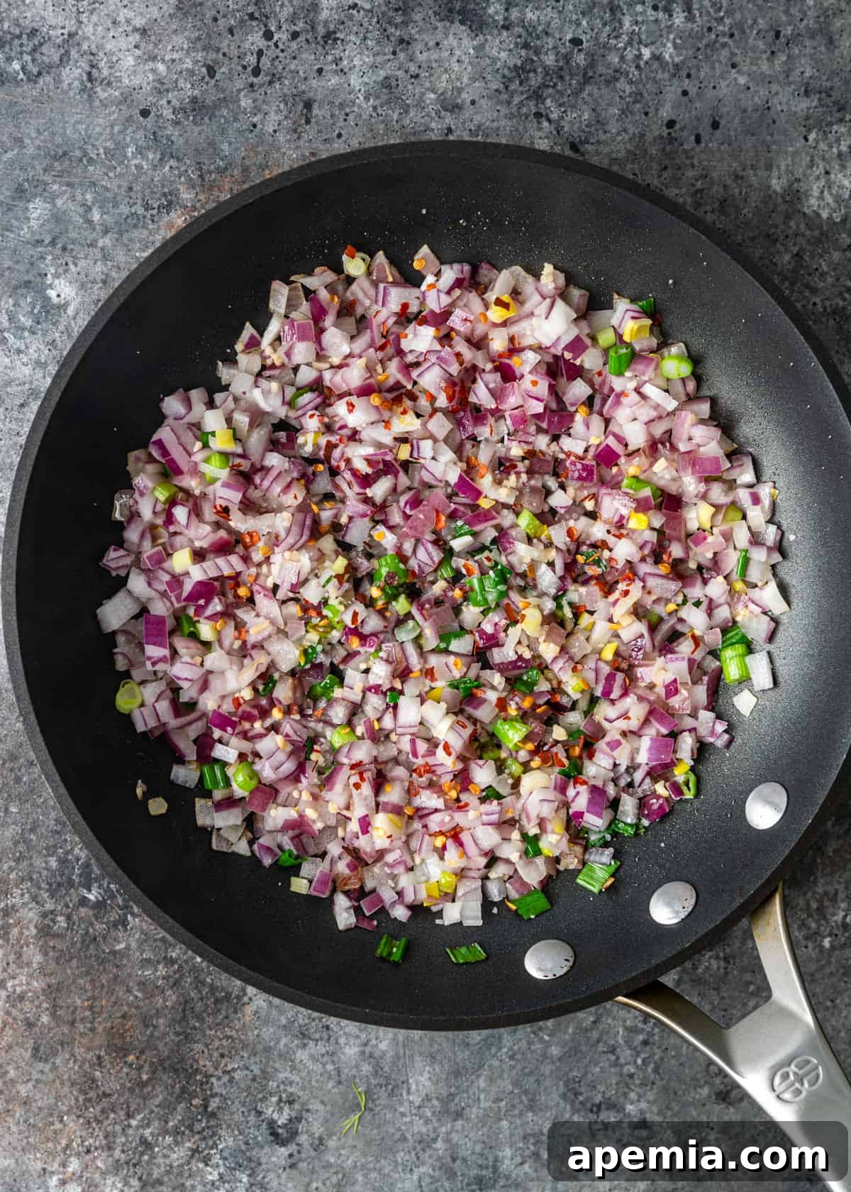 Overhead shot of diced red onions and minced garlic sautéing in olive oil in a skillet.