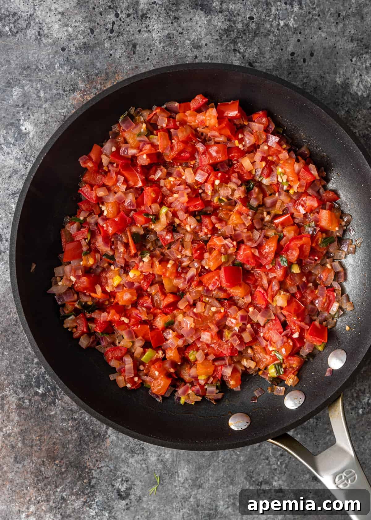 Overhead shot of diced tomatoes and red chili flakes being added to the sautéed onions and garlic in a skillet.
