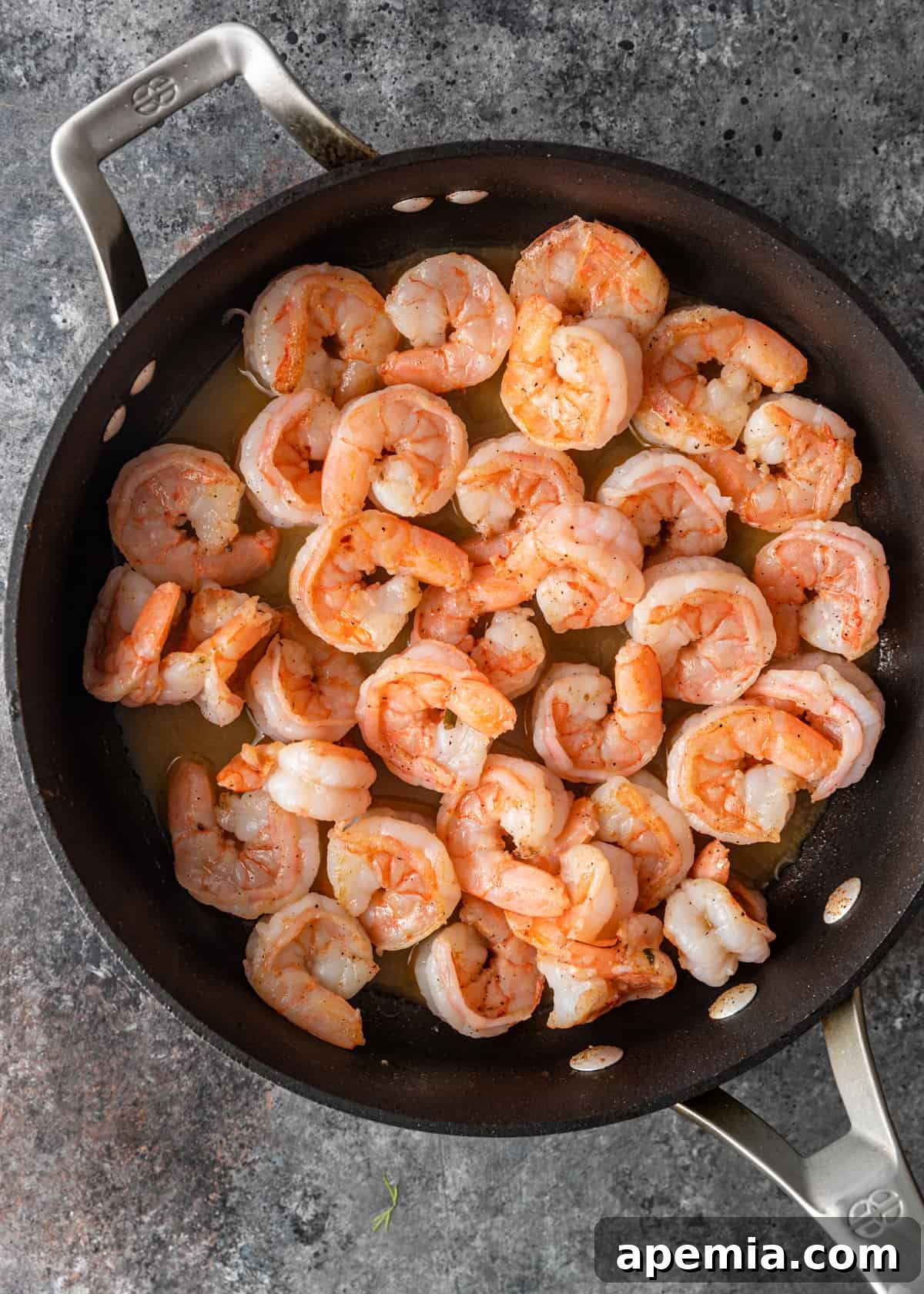 Overhead shot of shrimp cooking in a skillet, with ouzo being poured in to deglaze the pan.
