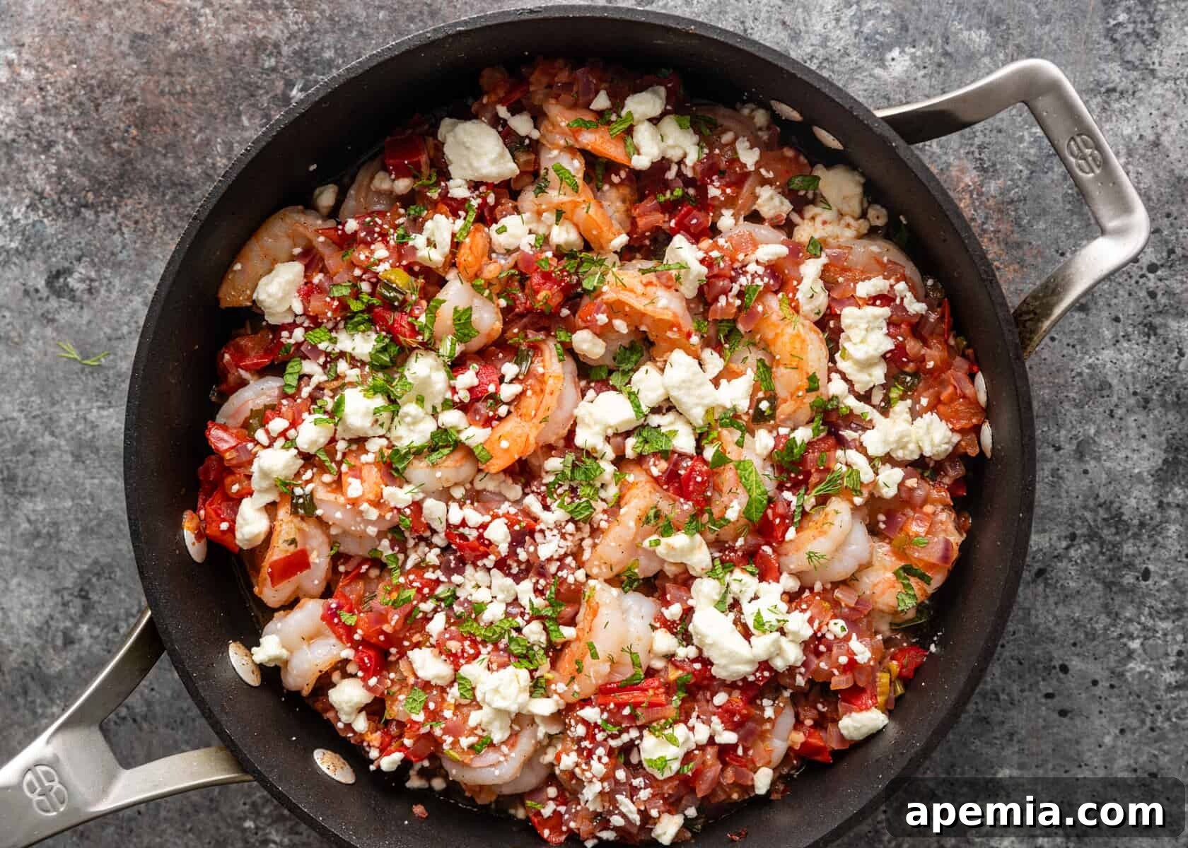 Overhead shot of Greek Shrimp Saganaki simmering in a skillet, with feta cheese and fresh herbs just added.