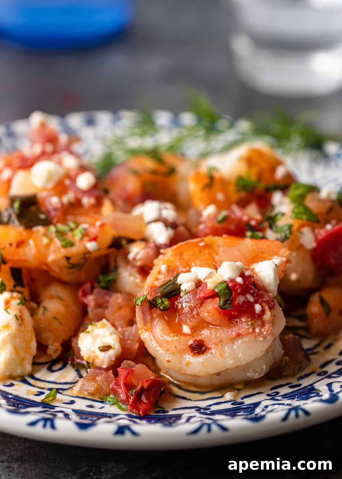 Close-up of a serving of Greek Shrimp Saganaki on a blue and white plate, featuring succulent shrimp, melted feta, and fresh herbs.