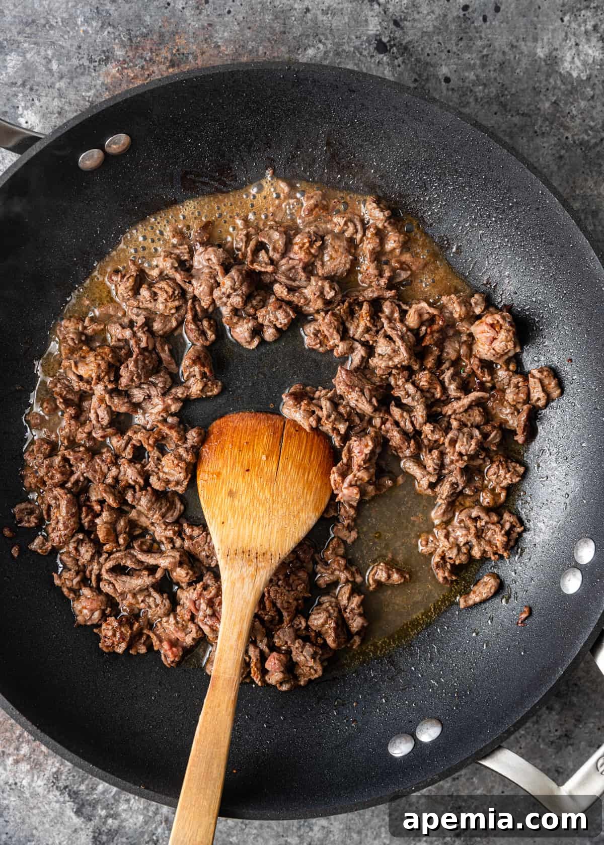 overhead: browning meat for tantuni in a skillet with a wooden spoon
