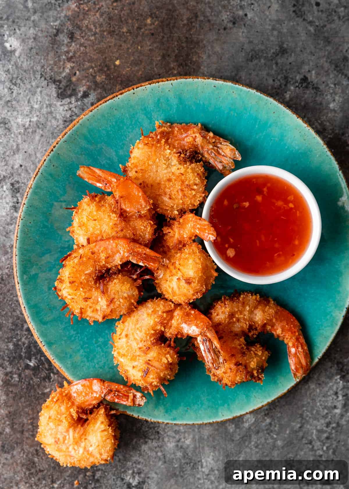 Sweet Coconut Crunch Shrimp 9 Overhead shot: a turquoise plate holds several crispy coconut shrimp and a small bowl of sweet chili sauce, perfectly arranged.