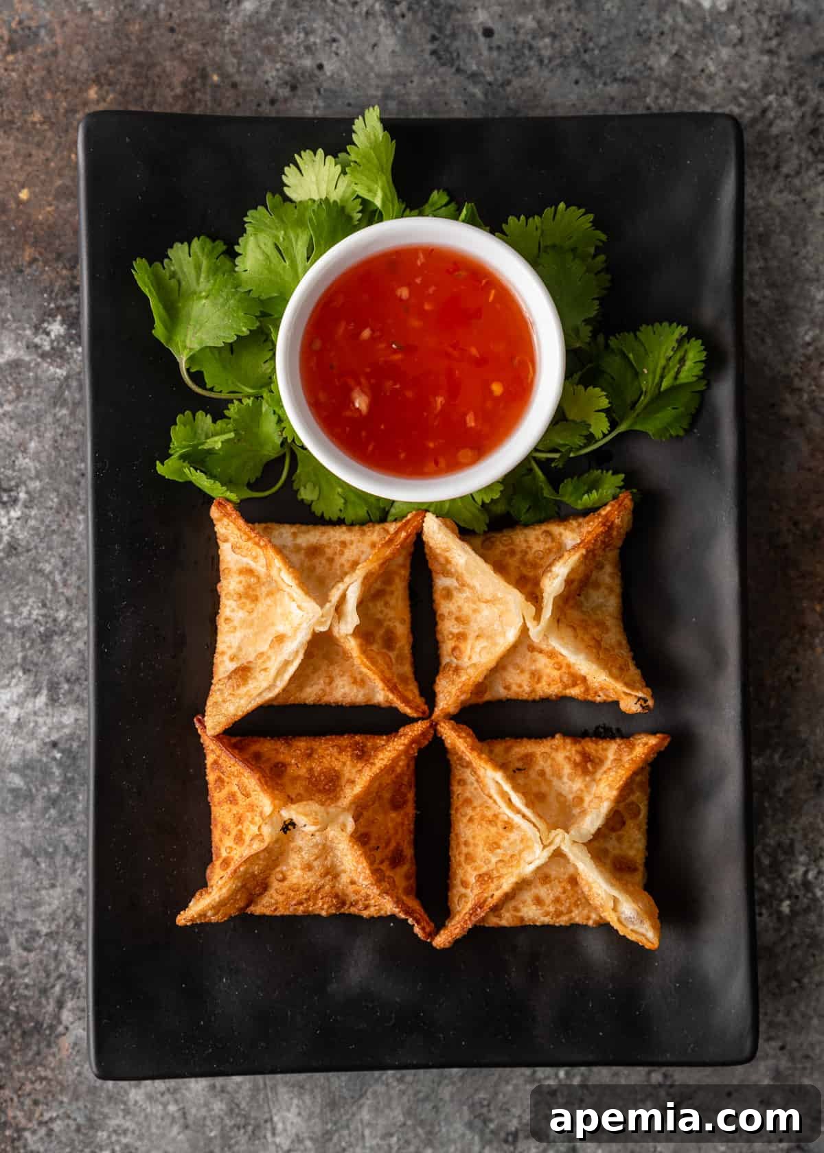overhead view: crab rangoon on a black platter with dipping sauce