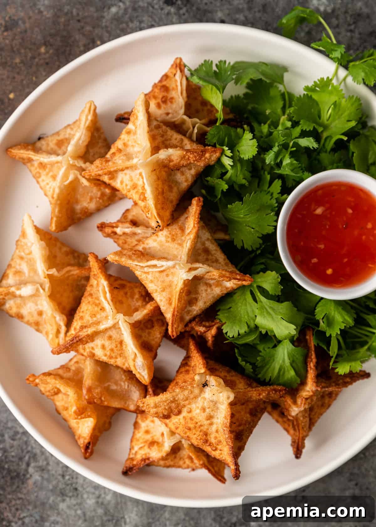 overhead: white plate with crab rangoons, side of dipping sauce and cilantro