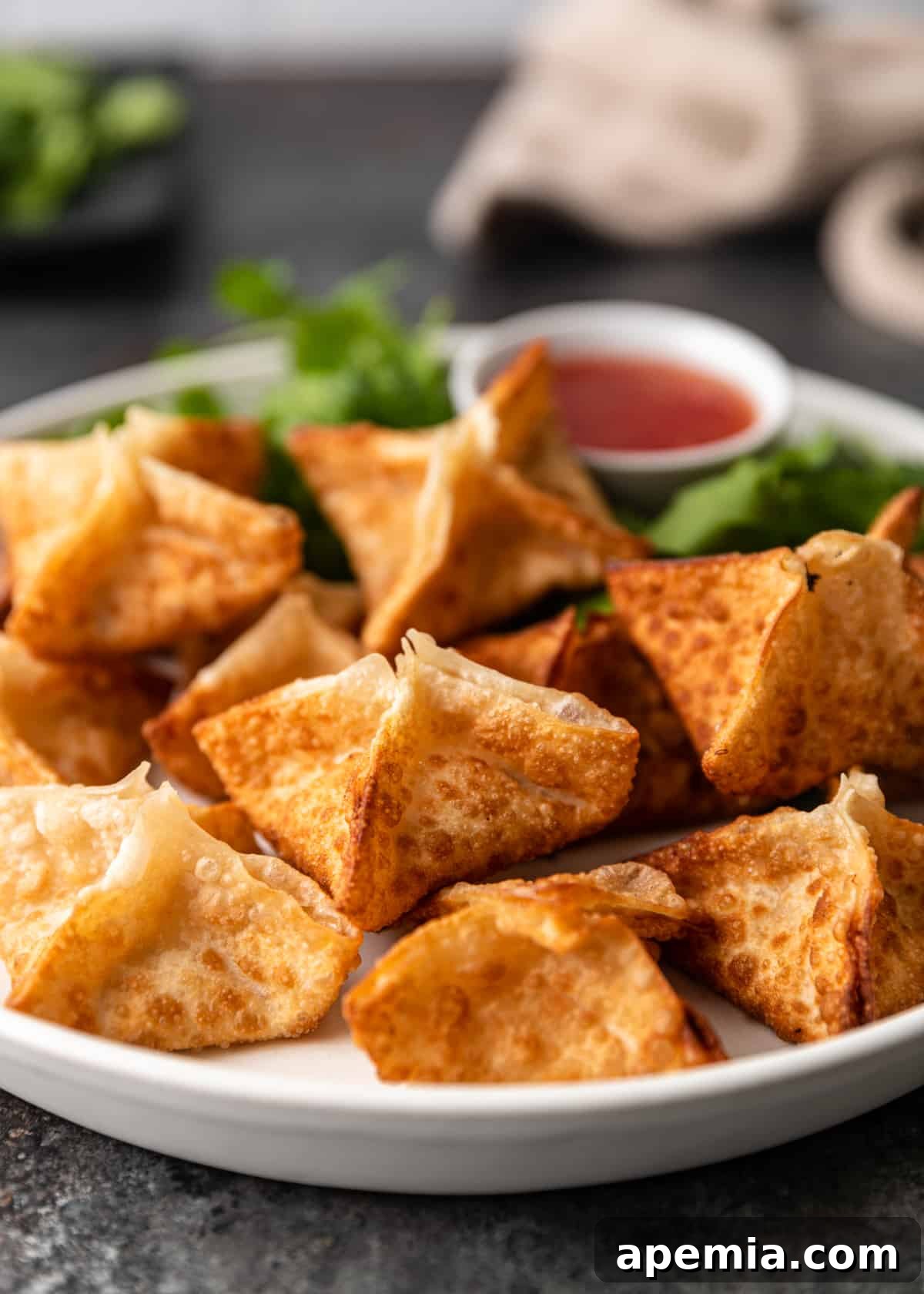 closeup side view: crab rangoon on a white plate sitting on table with side of dipping sauce